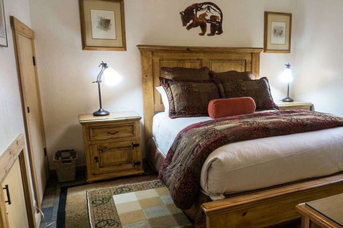Un dormitorio con una cama de madera, dos mesitas de noche con lámparas, una alfombra y un adorno de oso en la pared.