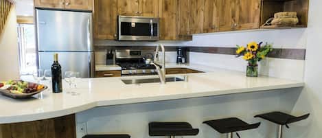 A modern kitchen with wooden cabinets, stainless steel appliances, a central island with bar stools, and a vase of flowers.