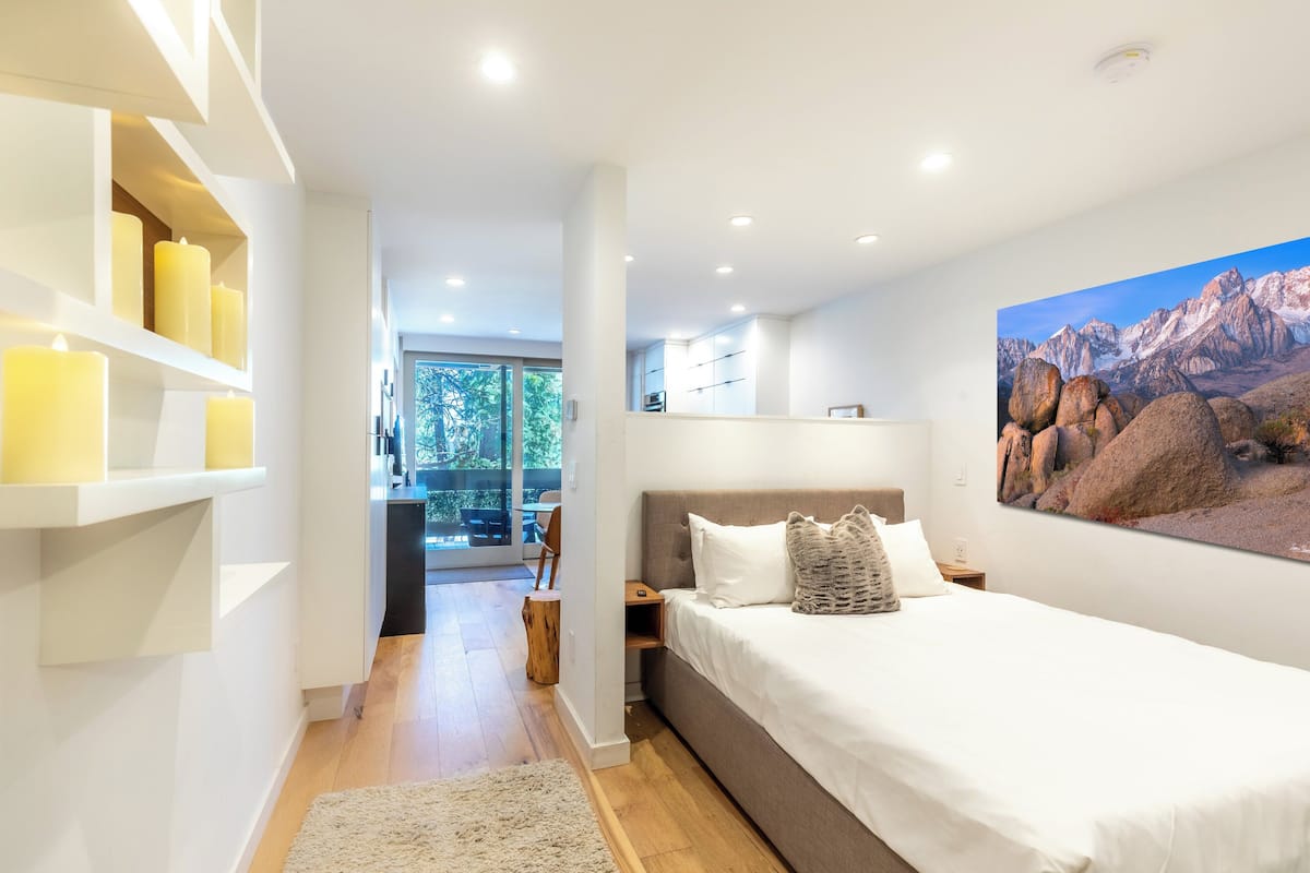 Un dormitorio moderno con una cama grande, un cuadro de montañas y vistas a un balcón.