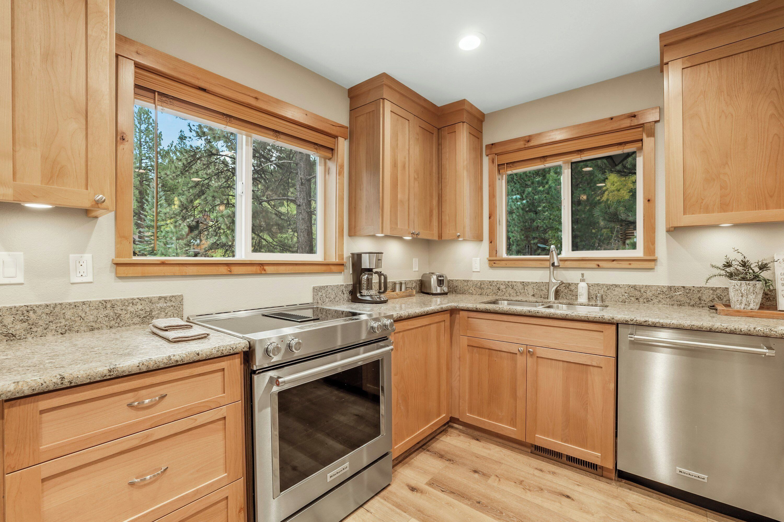 A modern kitchen with wooden cabinets, granite countertops, stainless steel appliances, and large windows.