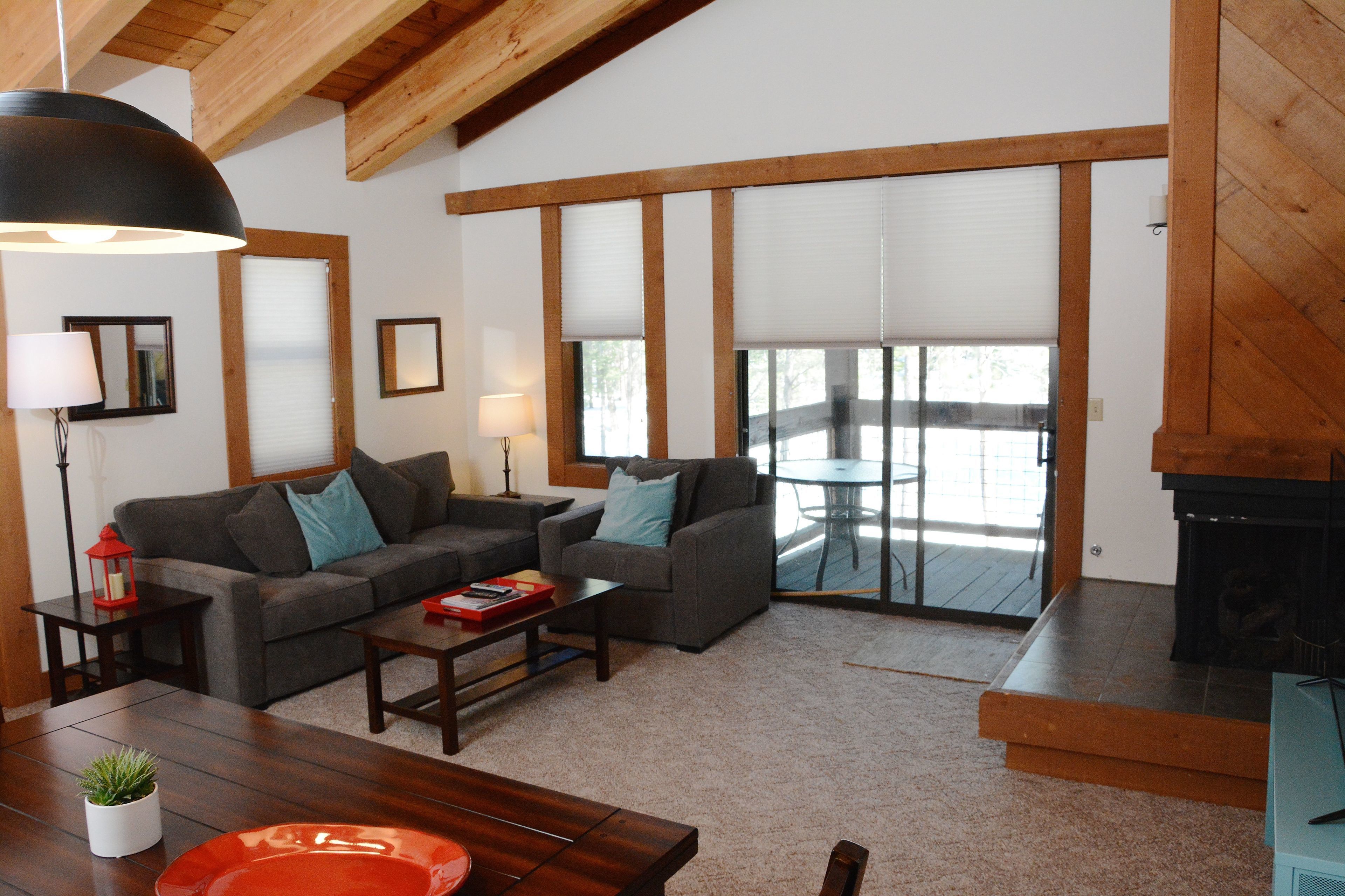 A living room with a sofa, coffee table, and fireplace. There is a dining table with chairs and a potted plant.