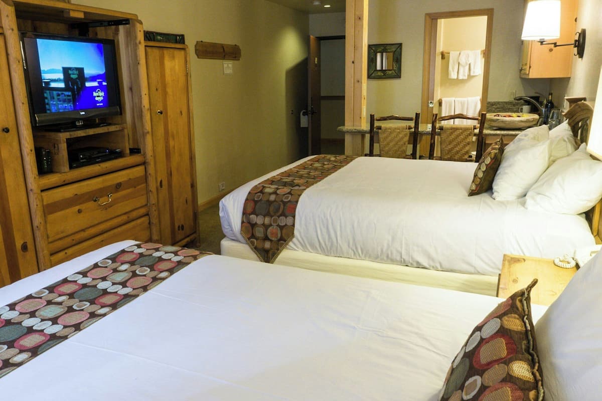 Habitación de hotel con dos camas, un aparador de madera y un televisor, y un baño visible a través de una puerta abierta.