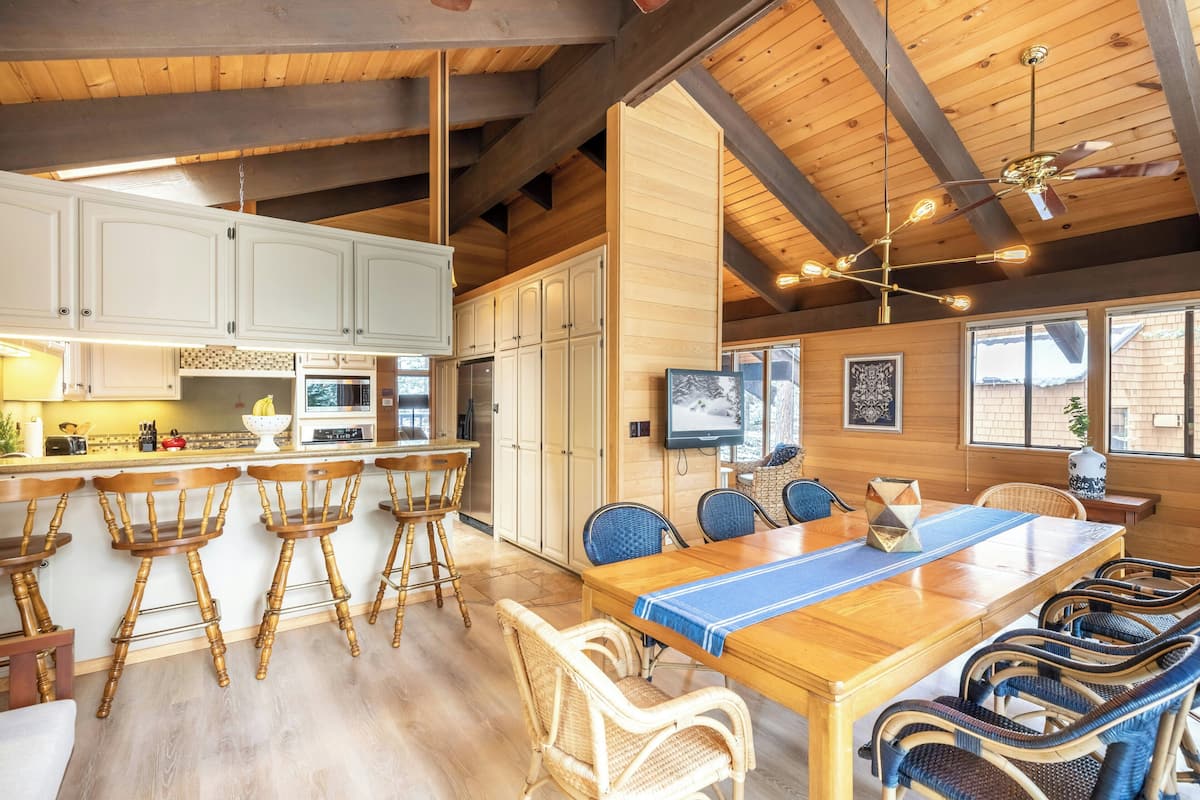 Una cocina amplia con armarios de madera, un comedor con una mesa larga y sillas, y una barra con taburetes.