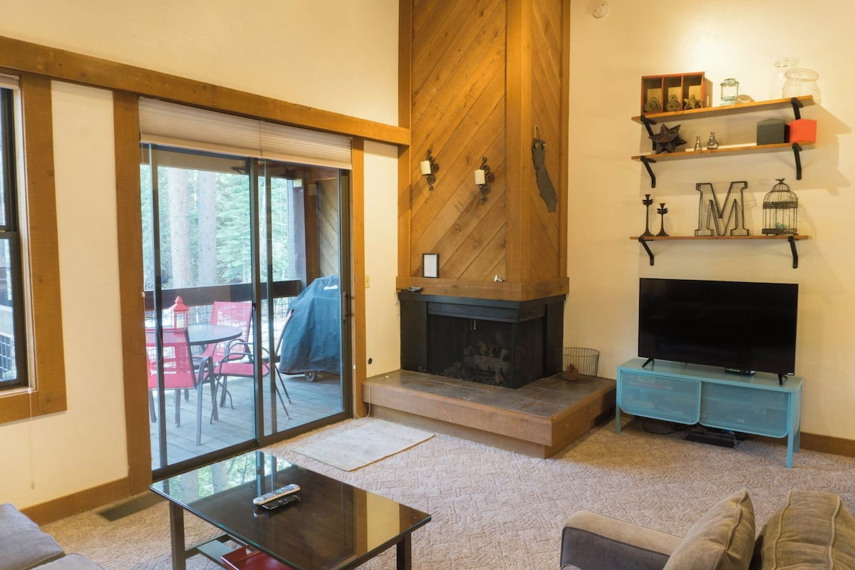 Una sala de estar con chimenea, un televisor sobre un mueble bajo y un ventanal corredero que da a un espacio al aire libre.