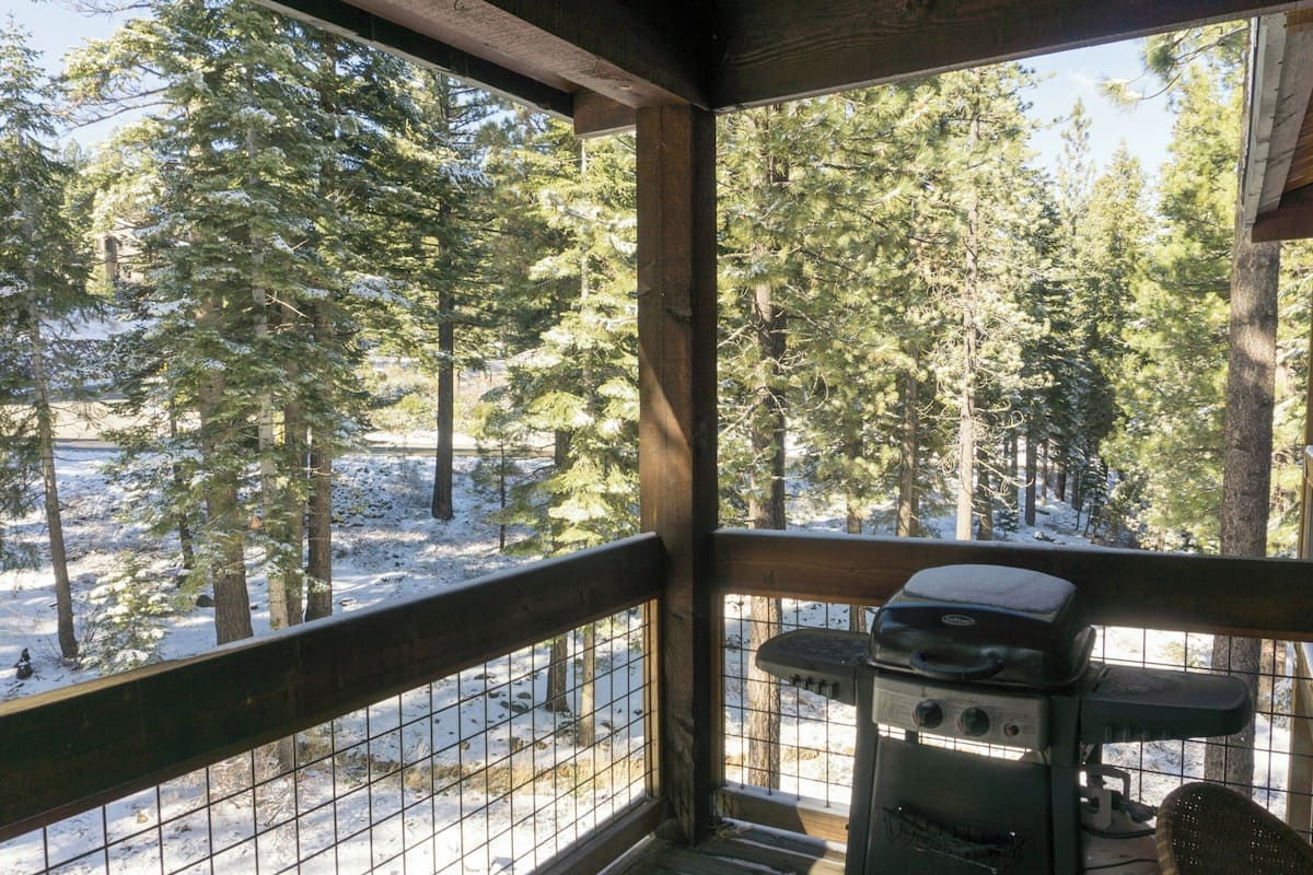 Una terraza de madera con una parrilla y vistas a un bosque nevado.