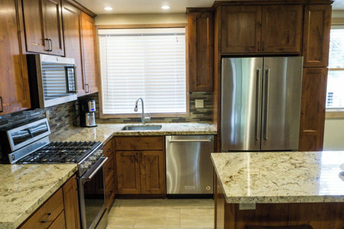 Una cocina con armarios de madera, electrodomésticos de acero inoxidable, encimeras de granito y lavavajillas.