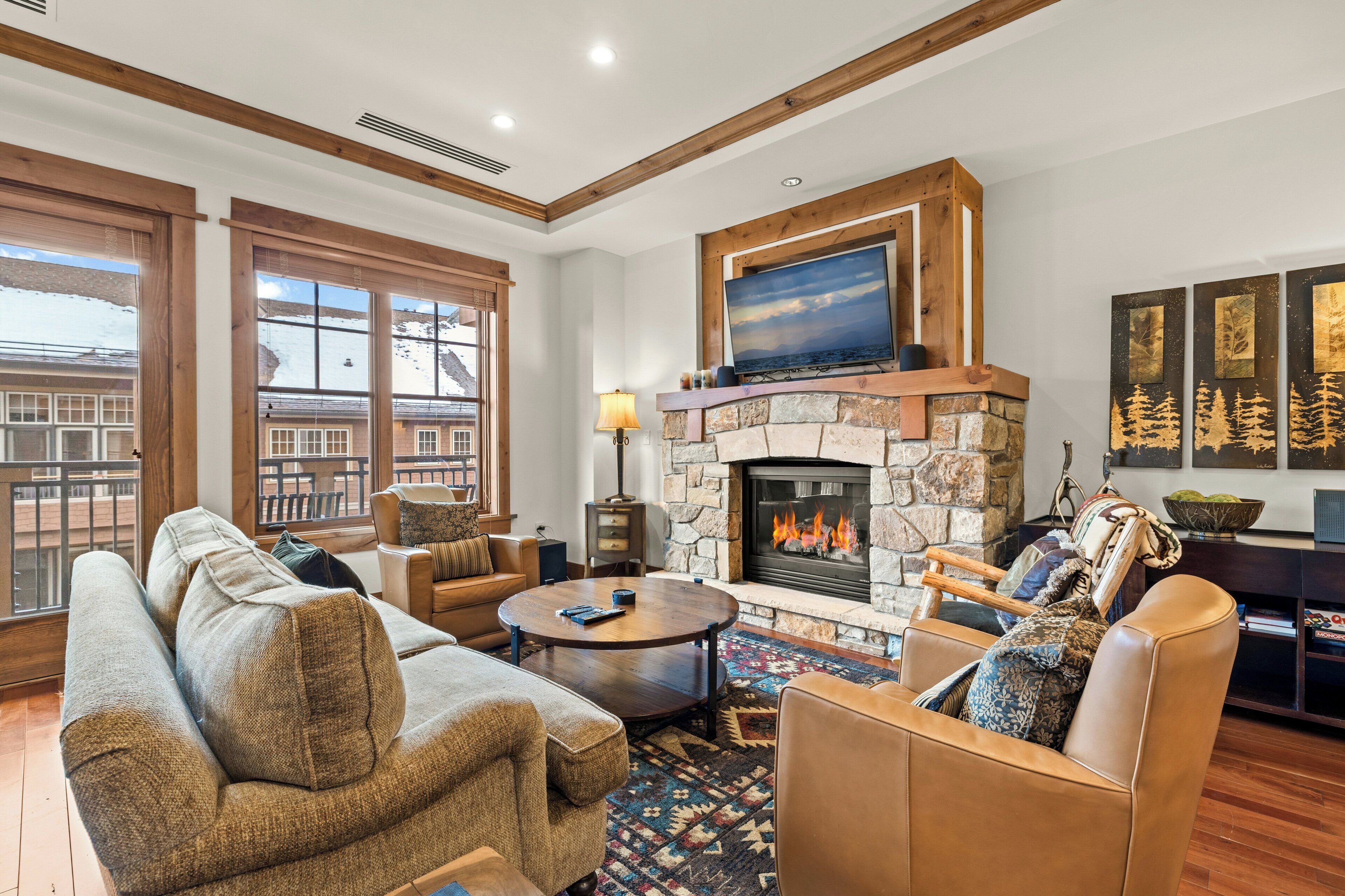 A living room with a stone fireplace, leather sofas, a round coffee table, and large windows.