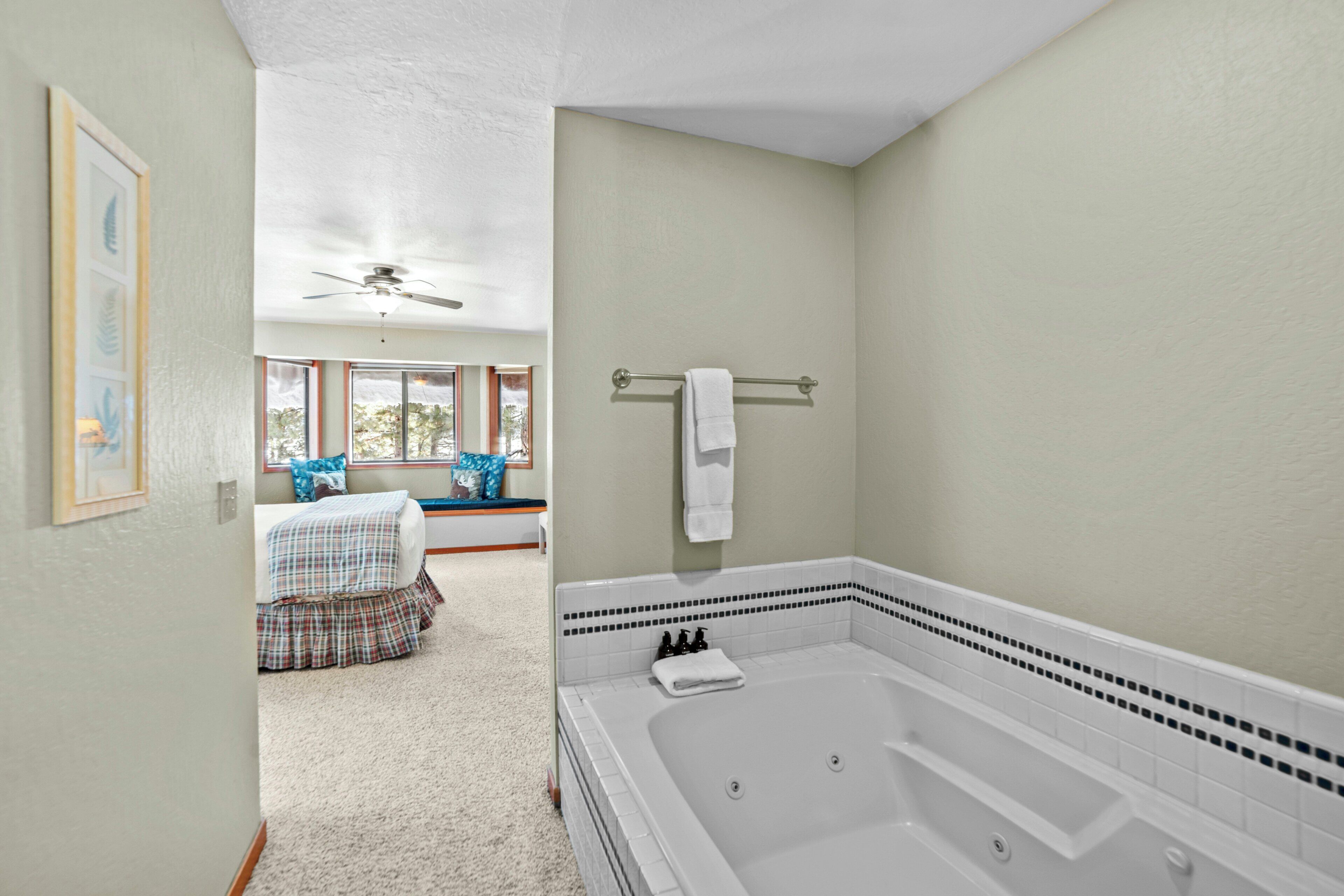 A bathroom with a large bathtub, a ceiling fan, and a window with a view of trees.