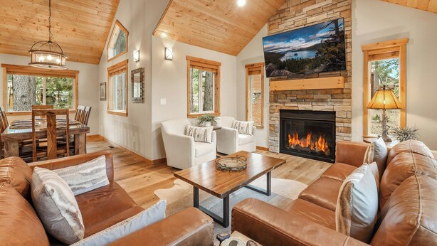 A spacious living room with a fireplace, leather sofas, a dining area with a wooden table, and large windows.