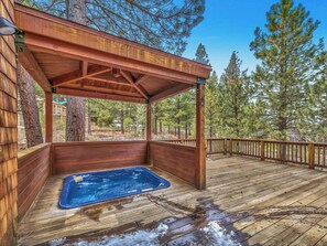 A wooden deck with a hot tub, surrounded by trees.