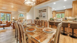 A spacious dining area with a large wooden table, multiple chairs, and a modern kitchen in the background.