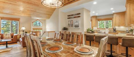A spacious dining area with a large wooden table, multiple chairs, and a modern kitchen in the background.