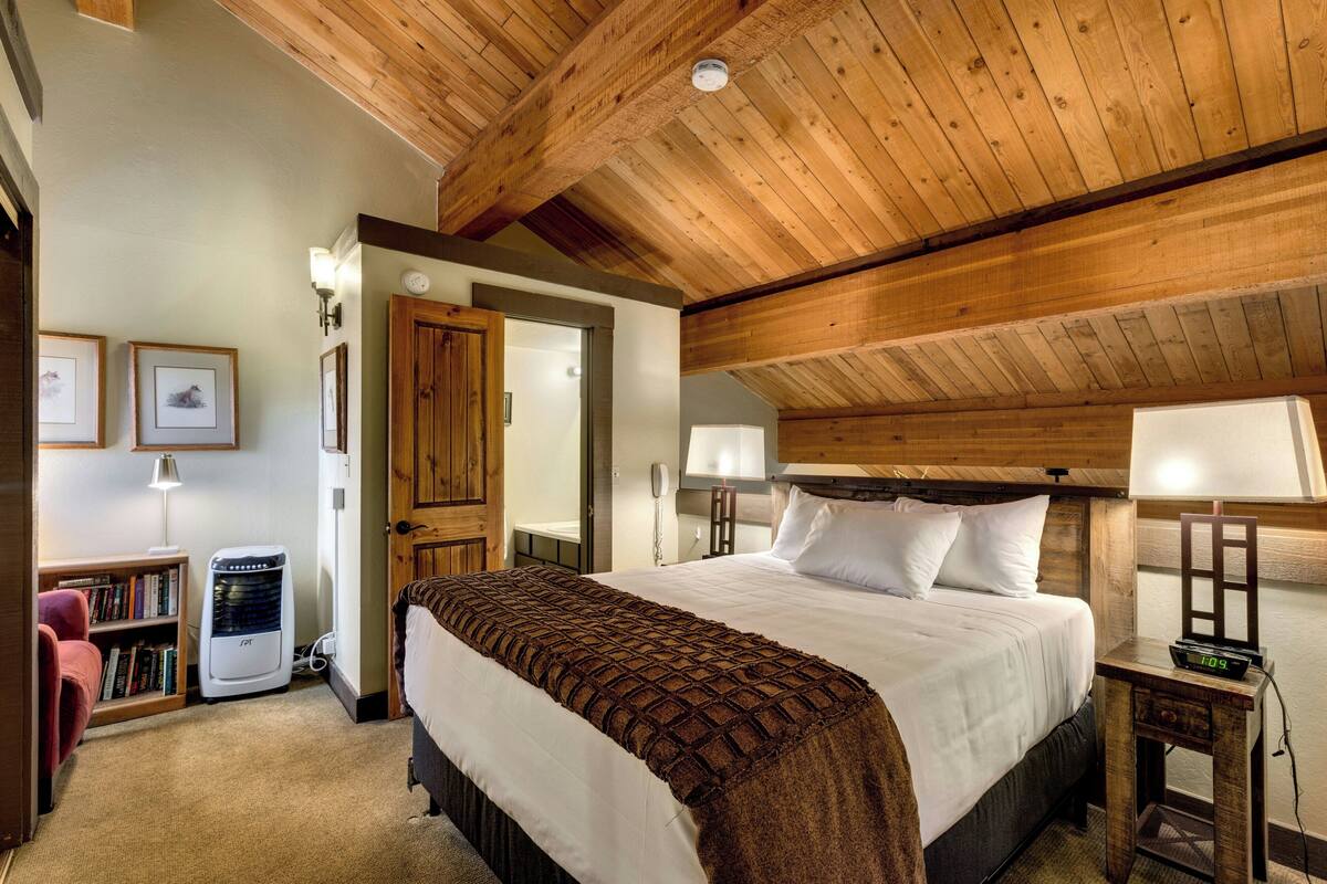 Un dormitorio con una cama grande, vigas de madera en el techo, un calentador, lámparas de noche y una estantería.