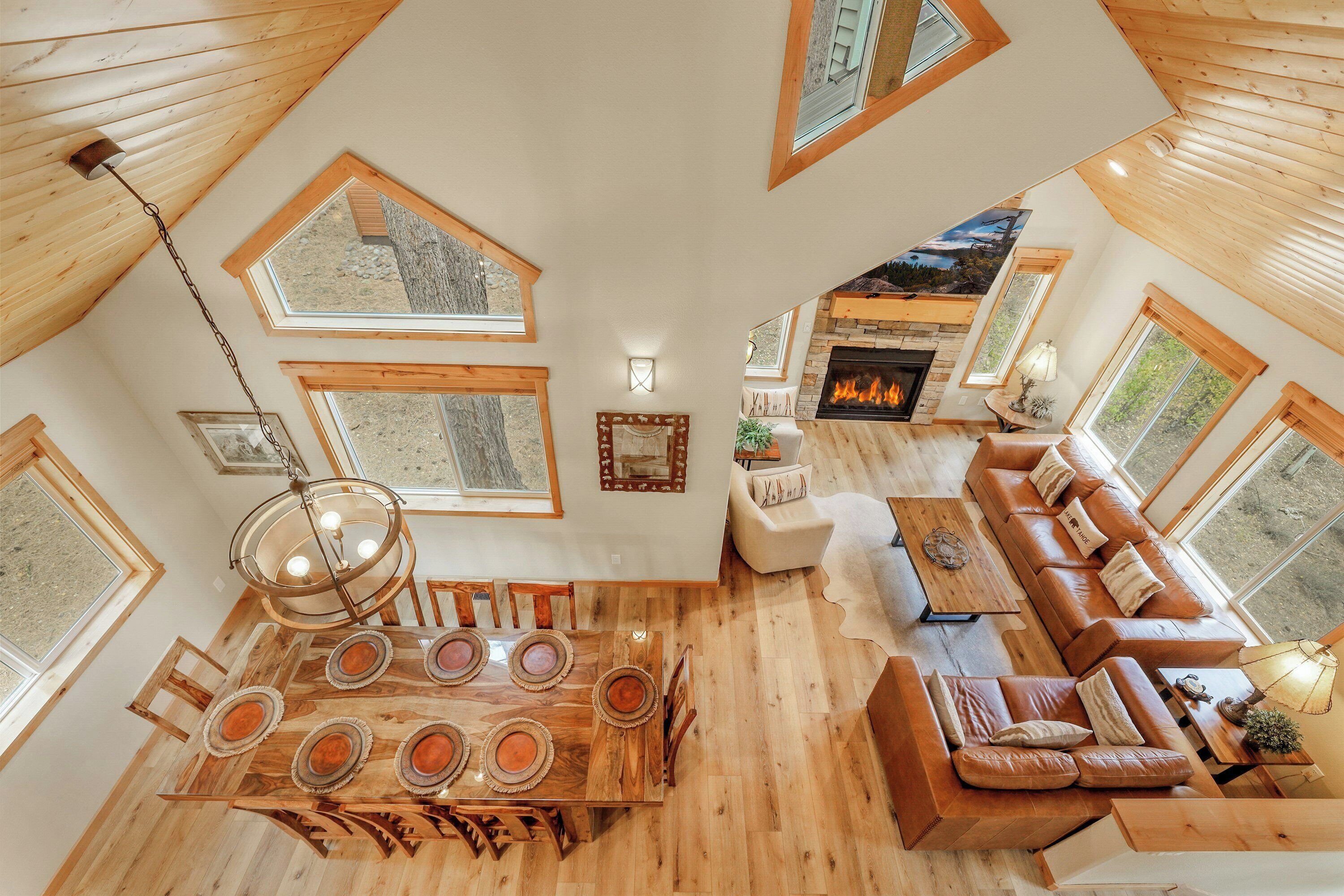 A spacious loft with a high ceiling, wooden beams, and large windows. It features a dining area with a wooden table and chairs, a leather sofa, and a fireplace.
