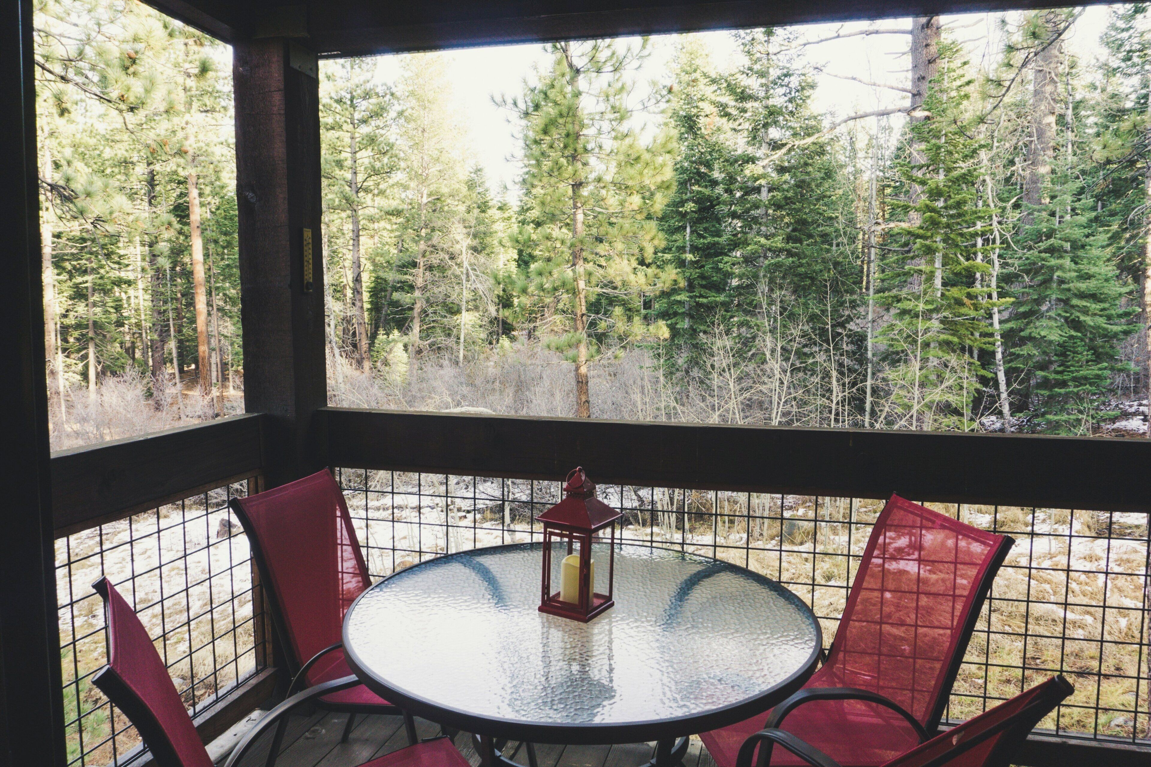 A round table with a glass top and four red chairs, a red lantern, and a view of a forest through a wire mesh window.
