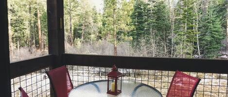 A round table with a glass top and four red chairs, a red lantern, and a view of a forest through a wire mesh window.