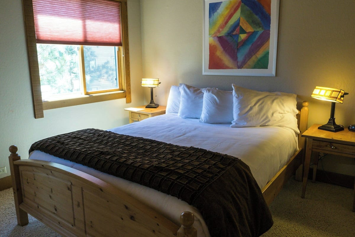 Una cama bien hecha con una colcha estampada, dos lámparas de noche, una mesita de noche y una ventana con persianas.