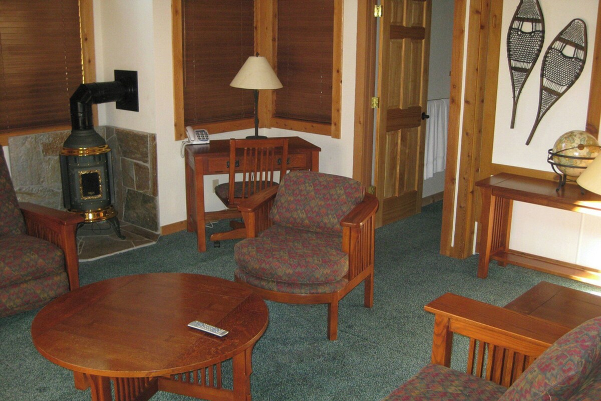 A cozy living room with a wood-burning stove, a round wooden table, and patterned armchairs.