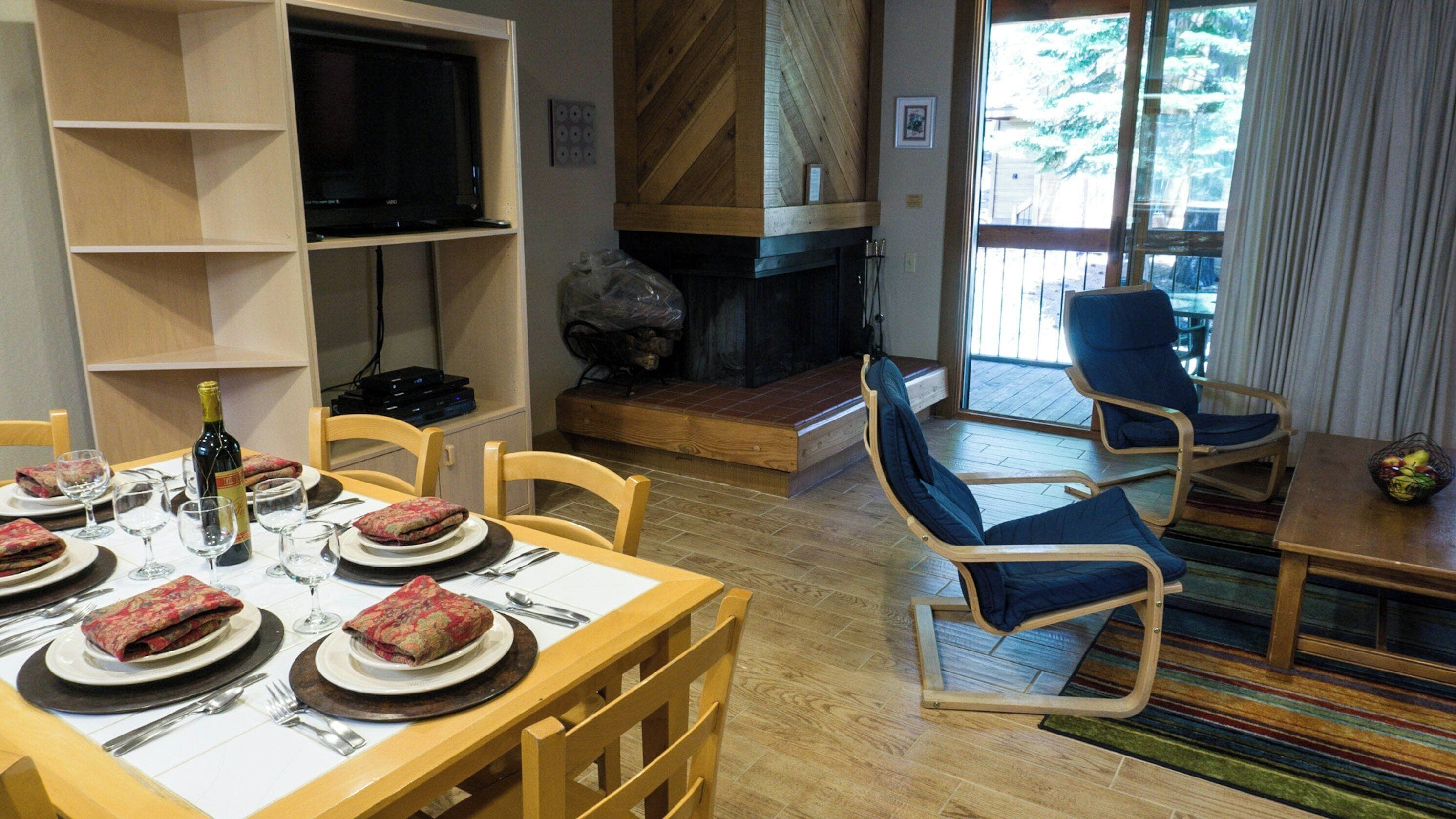 A dining area with a wooden table set for a meal, a television on a shelf, and a fireplace in the background.