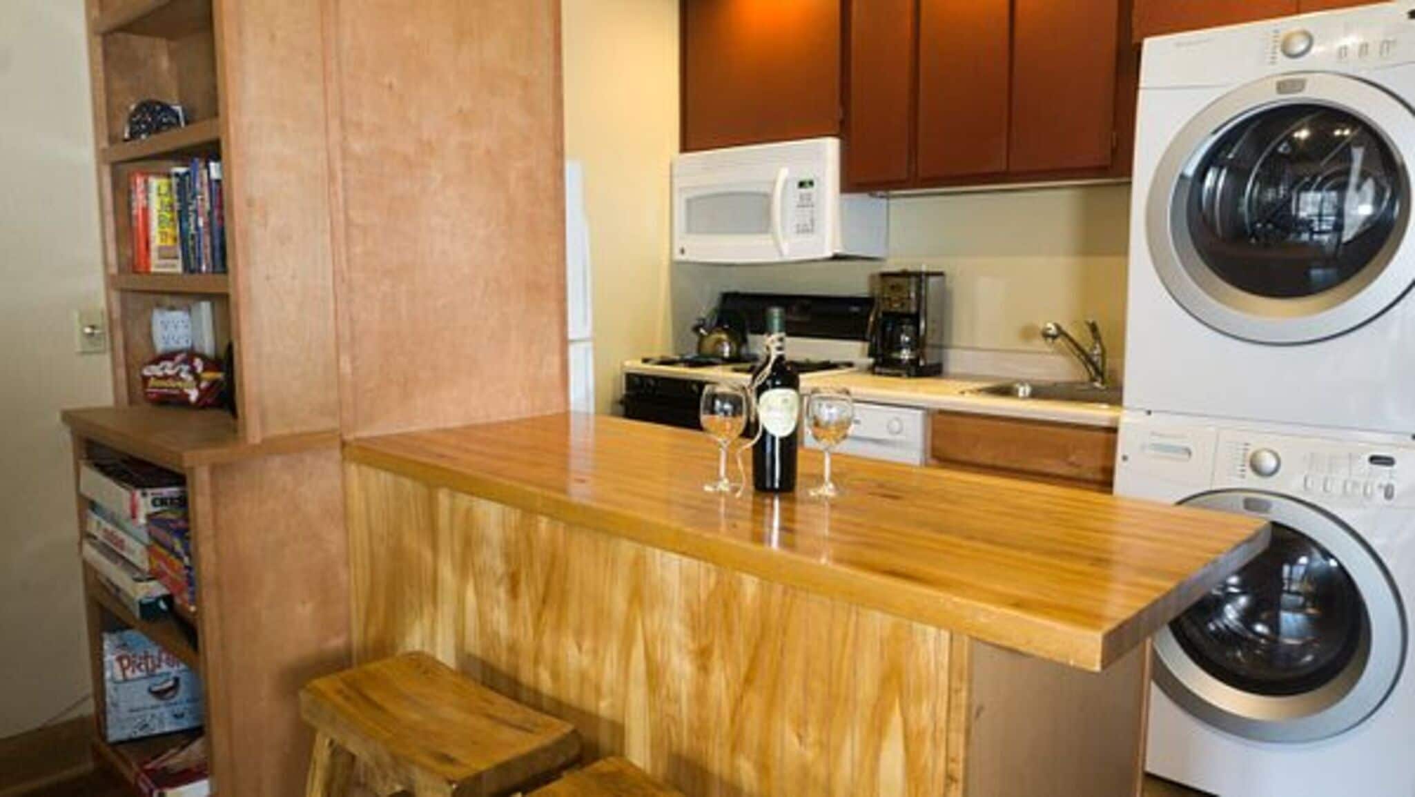 A compact kitchen with a wooden countertop, a microwave, a washing machine, and a small seating area.