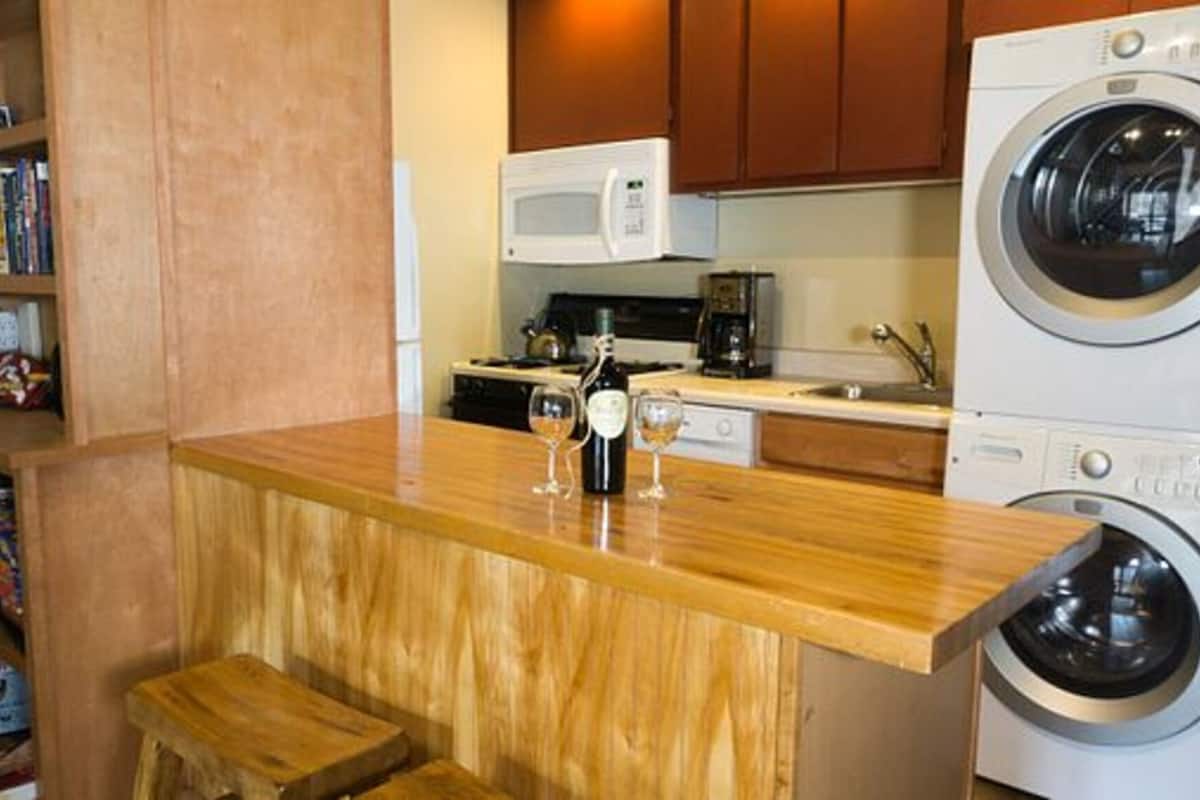 Cocina compacta con encimera de madera, microondas, lavadora y una pequeña zona de estar.