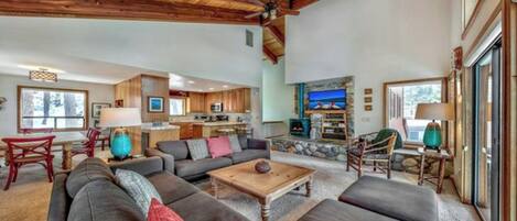 A spacious living room with a fireplace, a dining area with a table and chairs, and a kitchen in the background.
