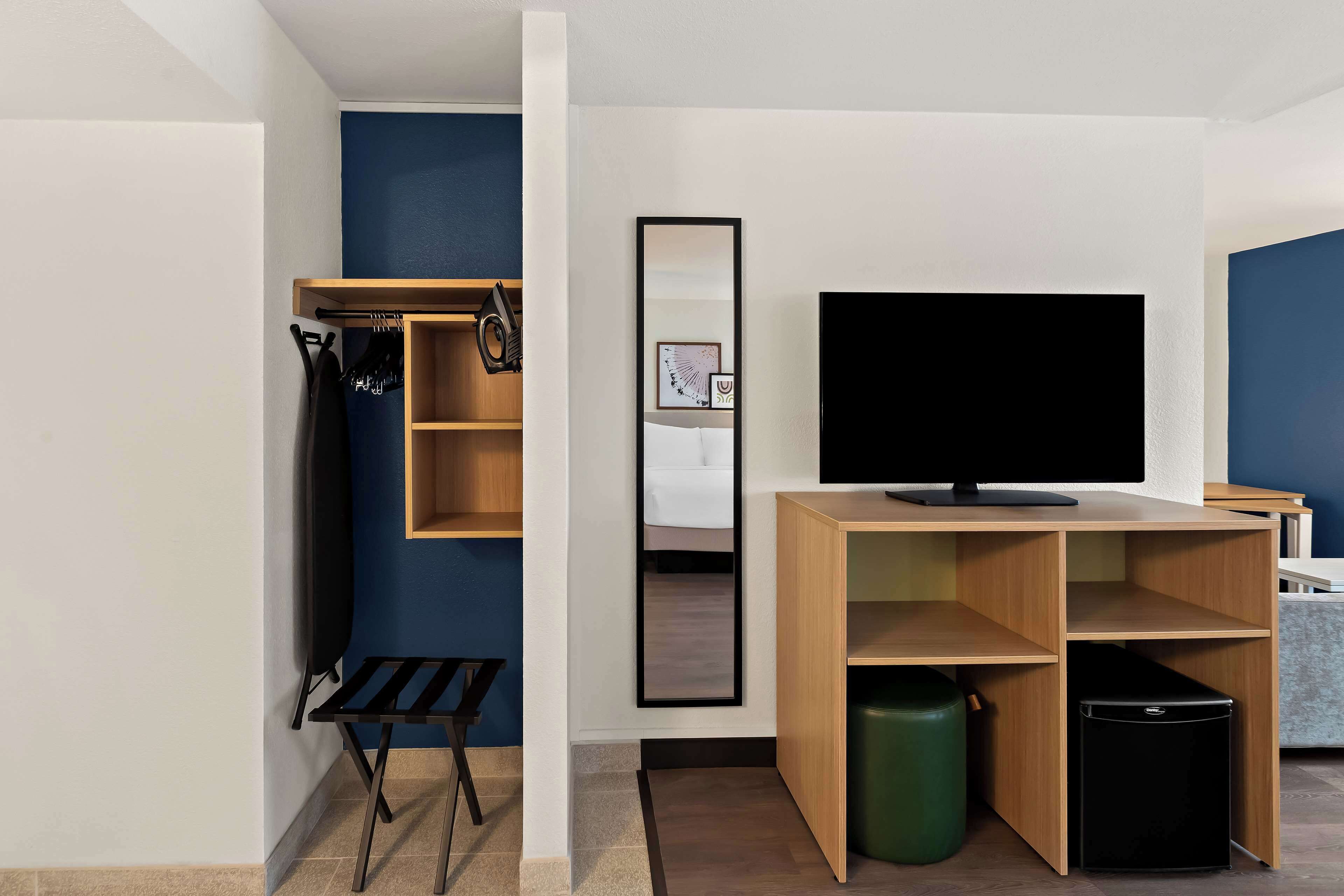 A modern room with a TV, a mirror, a small desk, and a bench.
