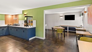 Una cocina moderna con armarios azules, una pared de acento verde y un comedor con sillas amarillas y una mesa.