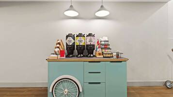 A teal cart with three coffee dispensers labeled Decaf, Regular, and Hot Water, and a small stack of books on top.