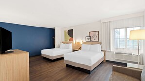 Una habitación de hotel con dos camas, televisión, escritorio y ventana con cortinas.