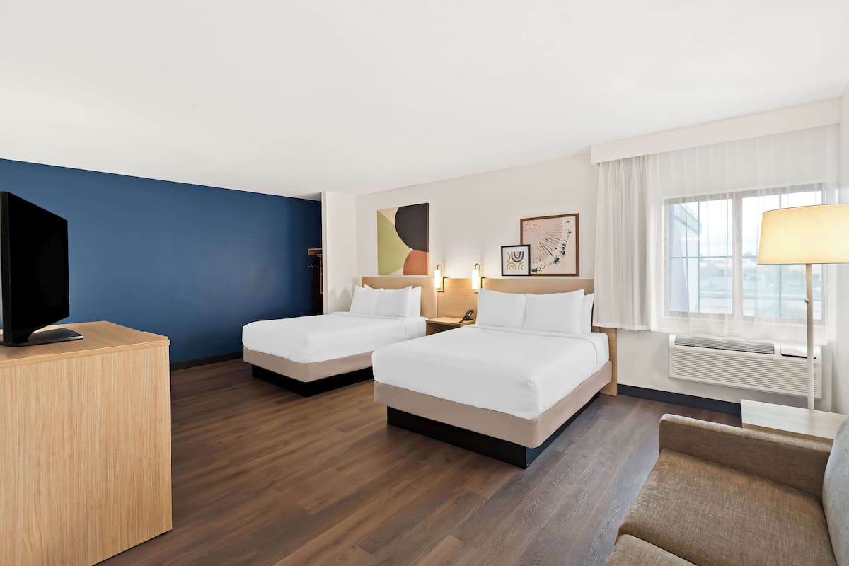 A hotel room with two beds, a TV, a desk, and a window with curtains.