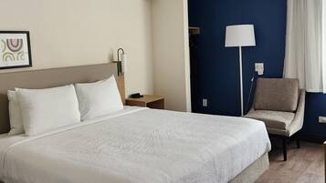 A hotel room with a large bed, a nightstand, a chair, a lamp, and a dark-colored wall.