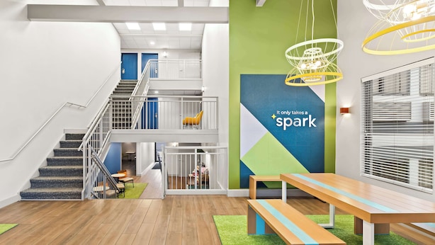 Un espacio interior moderno con una escalera, una pared verde y un letrero con la palabra 'spark', además de un banco de madera.