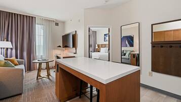 Habitación de hotel con escritorio, sofá, mesita, lámpara, televisor, espejo y obras de arte en la pared.