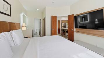 A hotel room with a large bed, a TV mounted on the wall, a bathroom with a toilet and sink, and a wooden headboard.