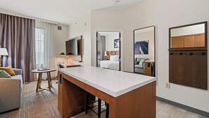 A hotel room with a desk, a sofa, a small table, a TV, and a mirror.