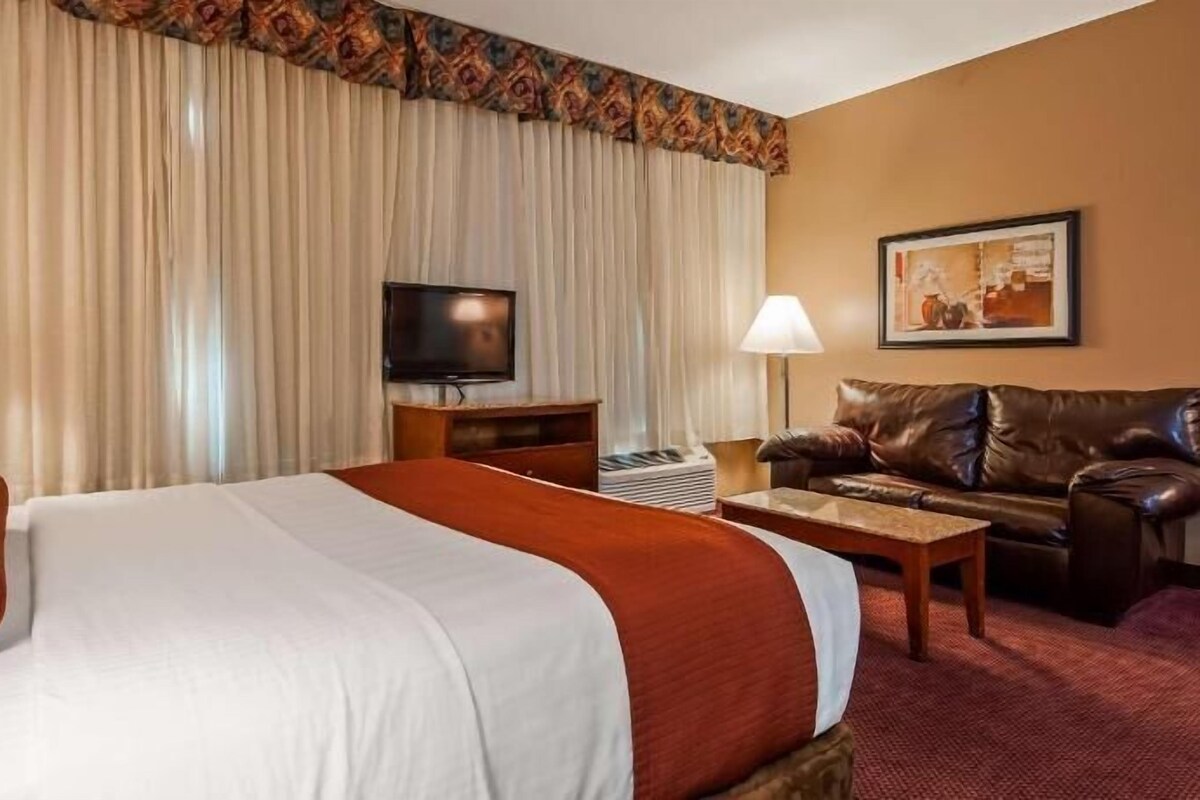 A hotel room with a bed, a television, a couch, and a painting on the wall.