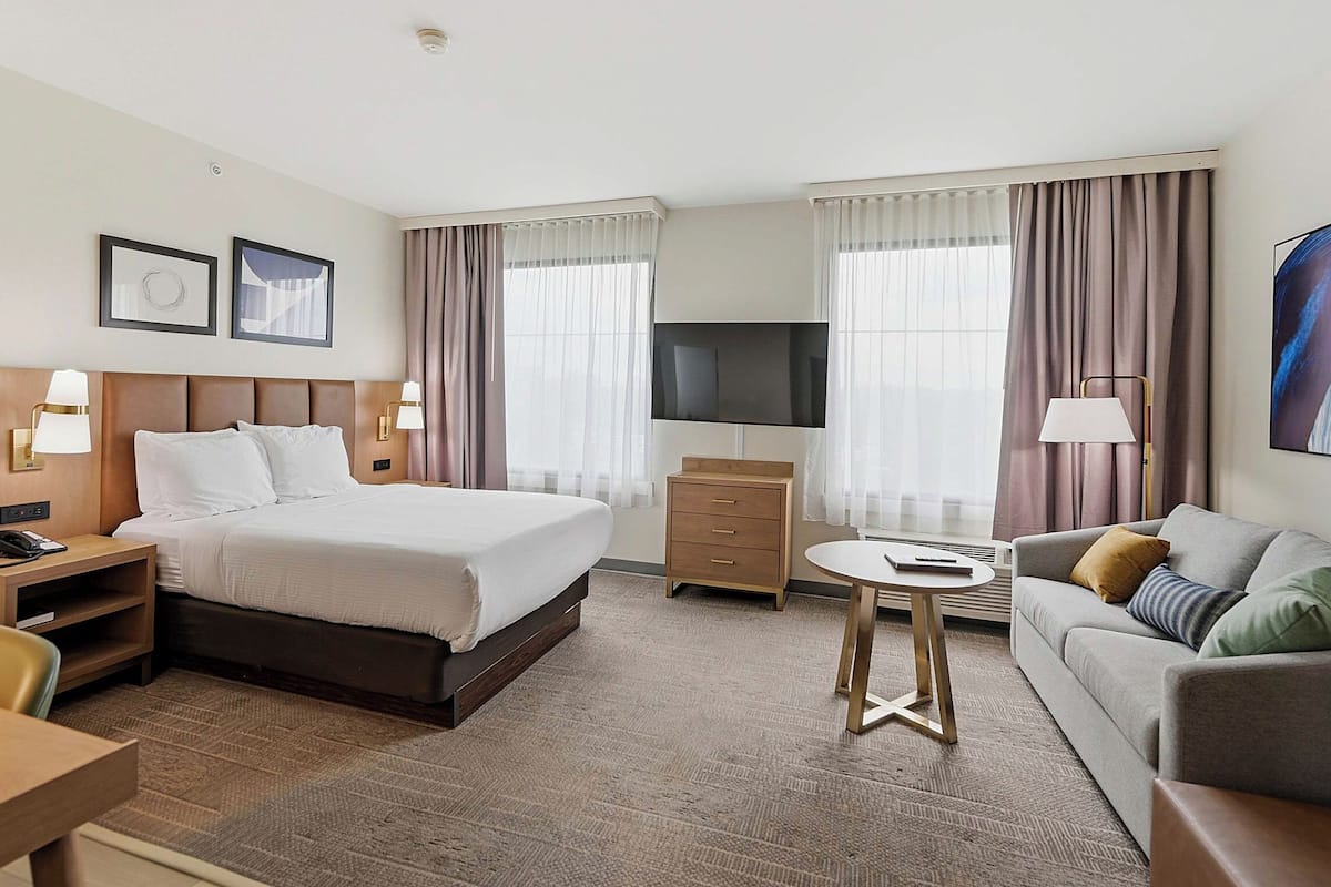 A hotel room with a bed, a sofa, a TV, a desk, and a chair.