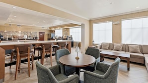 A modern hotel room with a dining area, a sofa, and large windows.