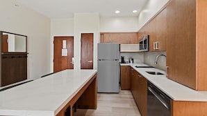 A modern kitchen with wooden cabinets, a stainless steel refrigerator, a microwave, and a dishwasher.