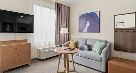 Une chambre d’hôtel équipée d’un téléviseur à écran plat, d’un canapé, d’une petite table, d’une commode, d’un climatiseur et d’un tableau au mur.. Best Western Plus Hannaford Inn & Suites