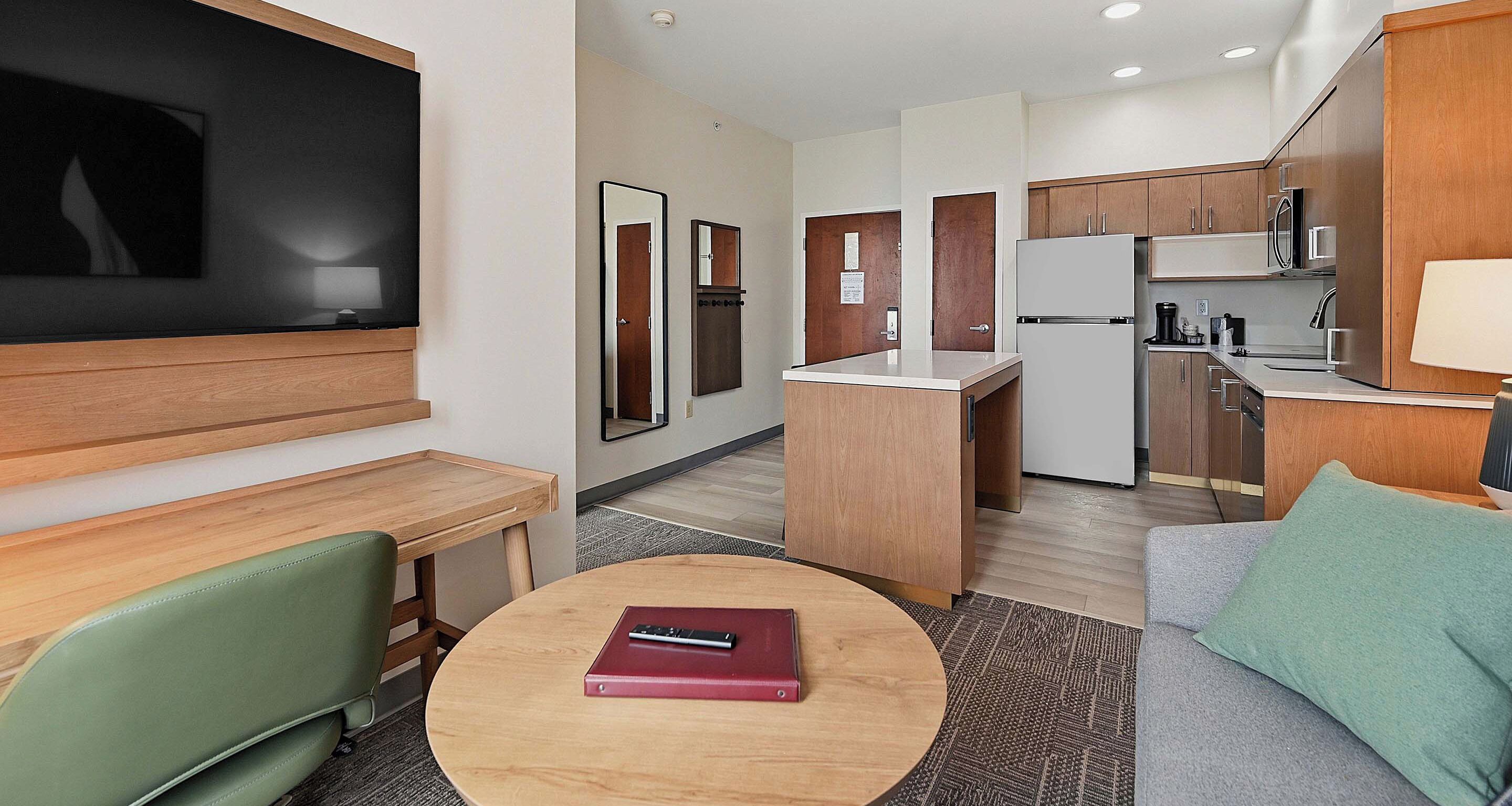 Quarto de hotel moderno com televisão, área de jantar, cozinha compacta e sofá.