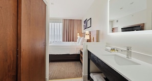 A hotel room with a bed, a bathroom with a sink and mirror, and a view of the outside through the window. - Best Western Plus Hannaford Inn & Suites (Cincinnati)