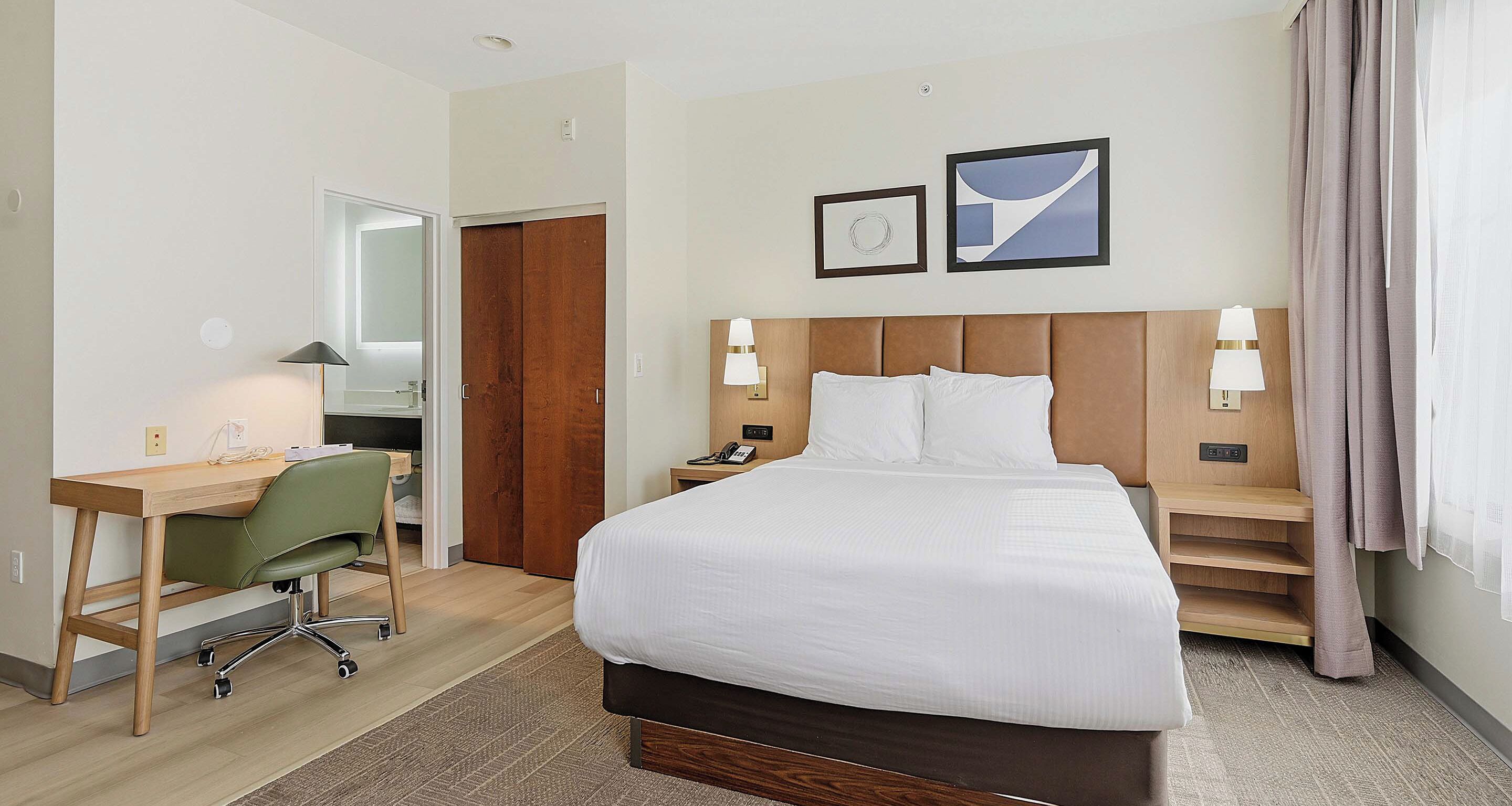 A hotel room with a bed, desk, chair, and a wardrobe.