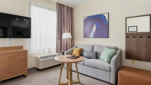 A hotel room with a flat-screen TV, a sofa, a small round table, a dresser, and a large abstract painting on the wall.