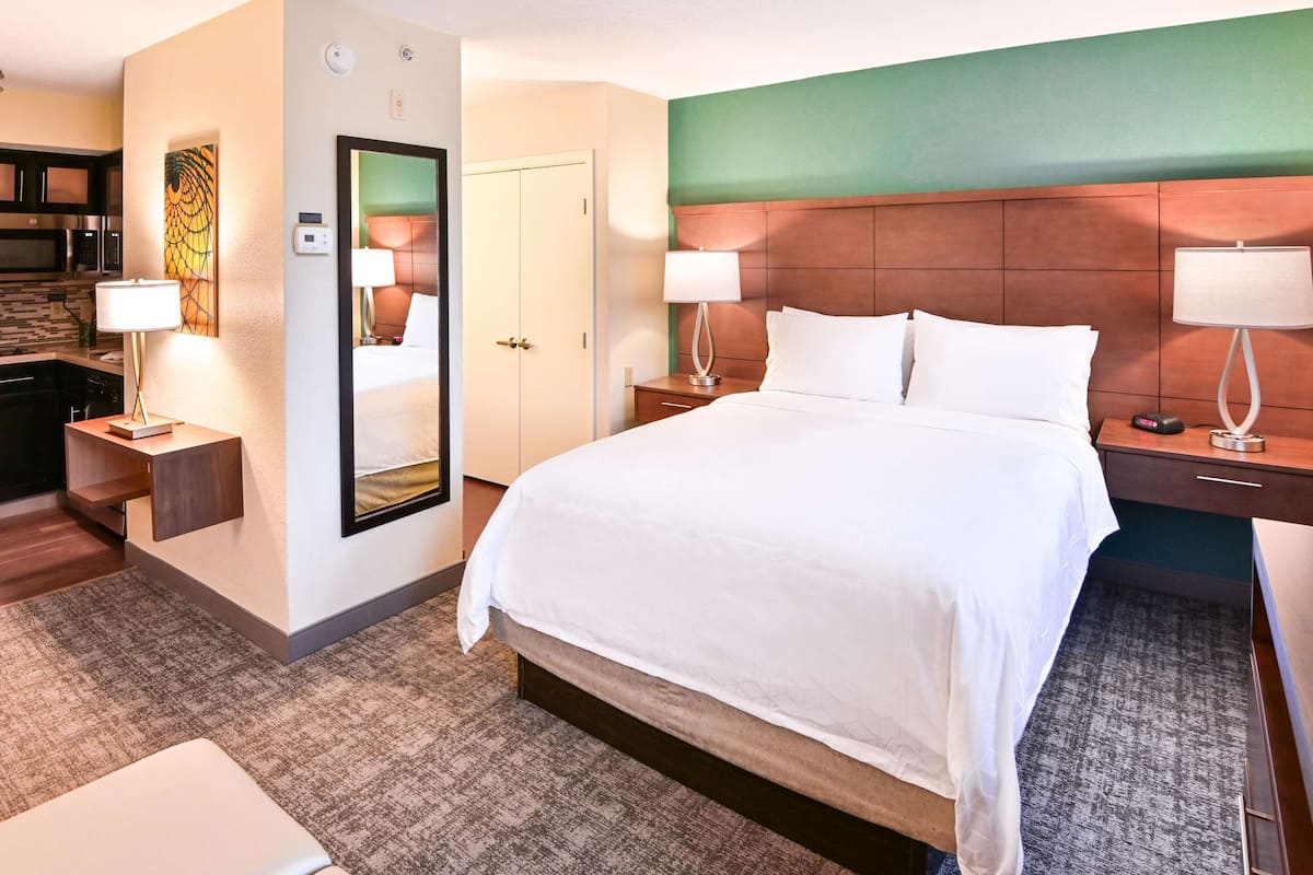 Een hotelkamer met een groot bed, twee nachtkastjes met lampen, een spiegel, een klein bureau en een magnetron in de kitchenette.