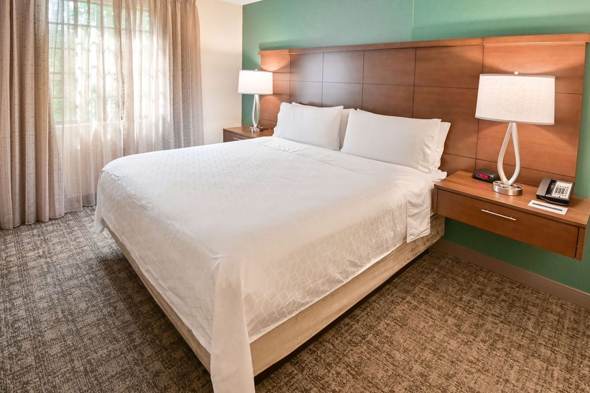 Hotelkamer met een groot bed, twee nachtkastjes, een lamp en een digitale klok.