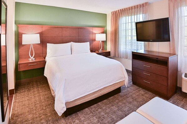 A hotel room with a large bed, two bedside tables with lamps, a TV on a stand, and a window with curtains.