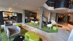A modern hotel lobby with seating areas, a staircase, and a breakfast area. - B&B HOTEL Mons Centre (Mons)