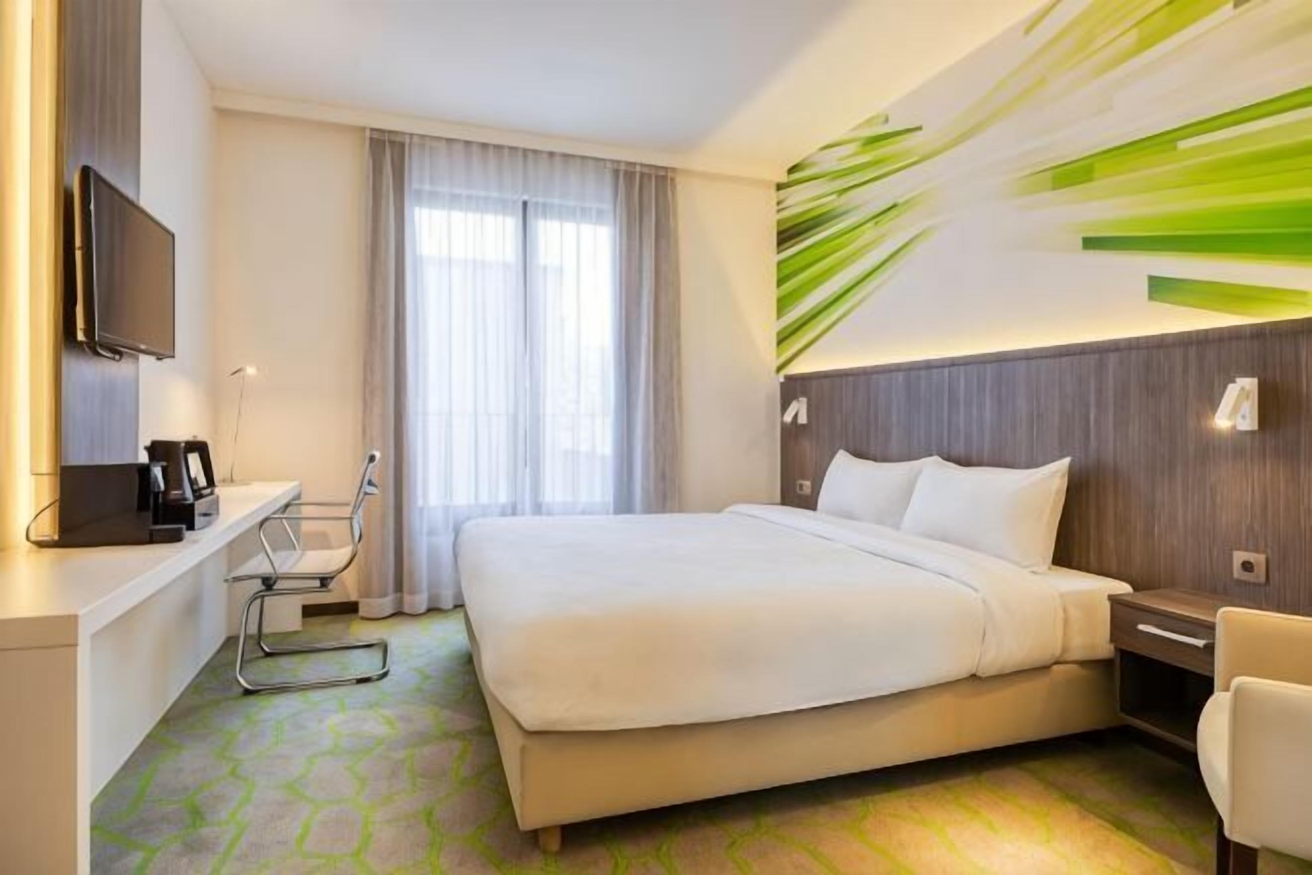 Una habitación de hotel con una cama, un escritorio con silla, un televisor y una ventana con cortinas.